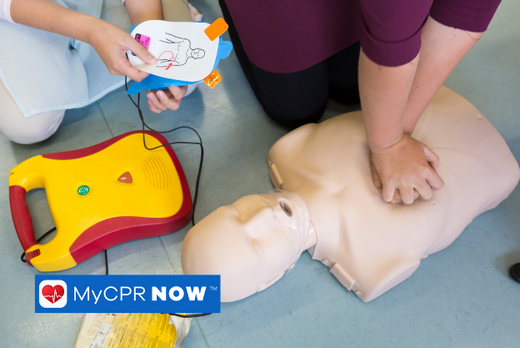 Someone practicing chest compressions on a CPR mannequin while someone else is setting up an AED.  