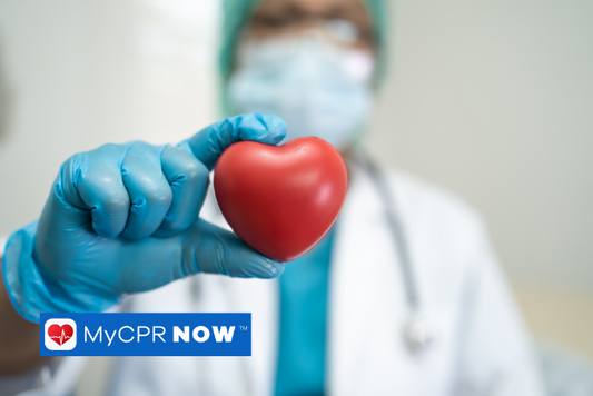 A medical professional wearing PPE holding up a red heart shaped object.