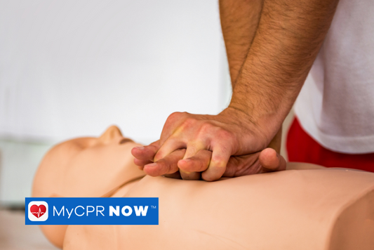 A close up of a mans hands performing CPR Chest compressions on an adult CPR mannequin. 