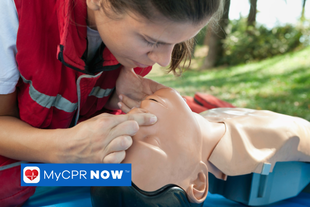 A woman performing rescue breaths during a training dummy in an outdoor setting.