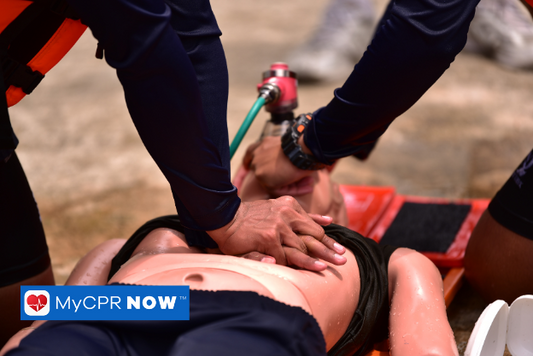 A person with a lifevest is performing chest compressions with a second person giving rescue breaths to the injuried person laying on their back.