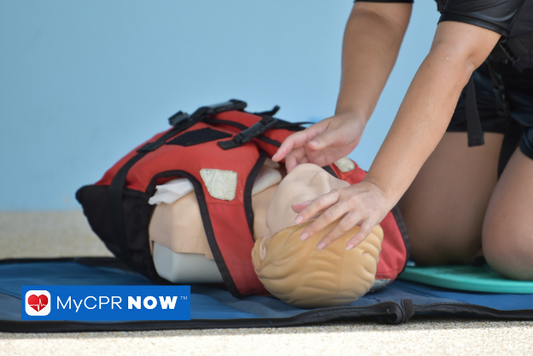 A person is performing Basic Life Saving CPR on a manikin training dummy with a water life safety vest