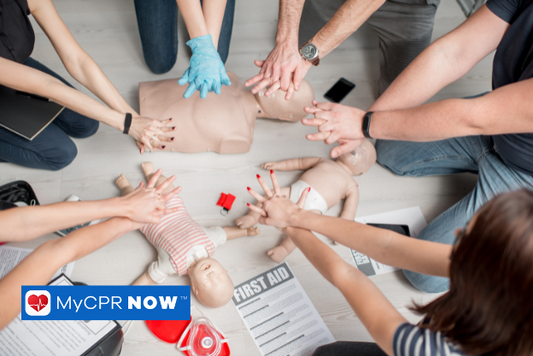 Multiple people are practicing CPR hand placement on adult and infant manikin training aids.