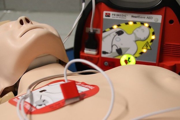 An adult CPR Mannequin with an AED pad on its chest and AED behind it. 